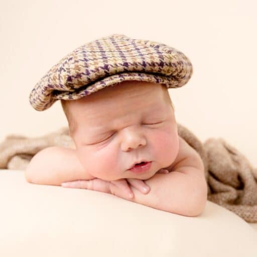 Newborn baby sleeping, wrapped in a white blanket on a cream background.